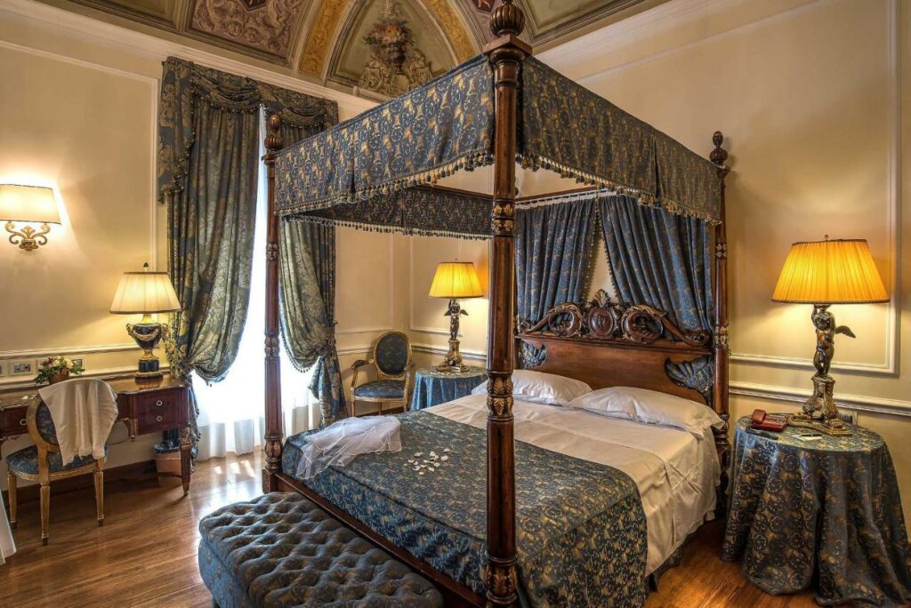 The canopy bed, the frescoes on the ceiling, the tapestries, the fabrics, and the wooden furniture in the hotel room.
